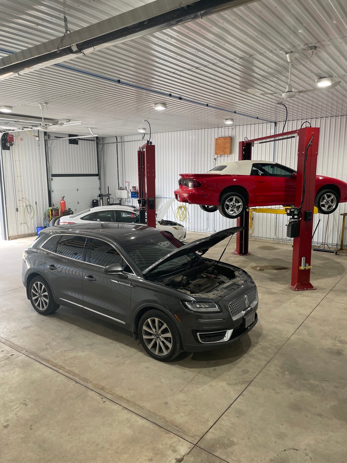 Inside the DUWYN Farm & Fleet shop: SUV with hood up beside a car on a two-post lift